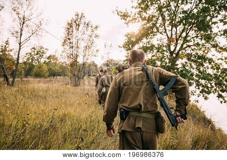 Group Of Reenactors Men Dressed As Russian Soviet Red Army Infantry Soldiers Of World War II Marching In Autumn Field With Weapons At Historical Reenactment.