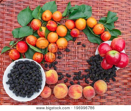 On the wicker table lie peaches and a branch with apricots plates with mulberry and apples.