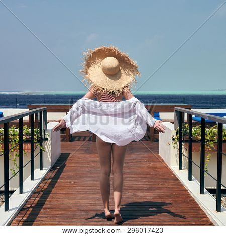 Woman in red striped one-piece swimsuit walking on tropical beach patio deck. Summer vacation at Maldives.