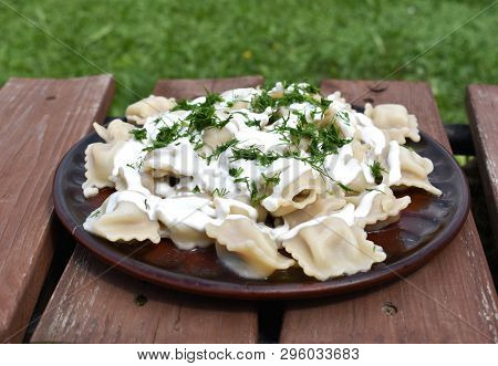 Dumplings With Sour Cream And Greens On A Wooden Table And Against Naturebackground.