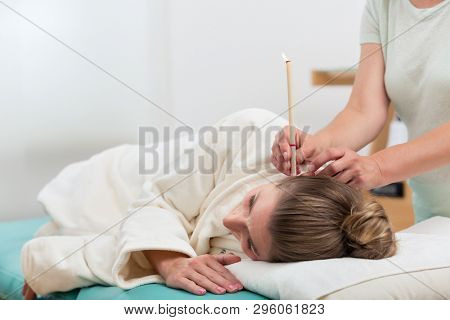 Close up of therapist hand with burning ear candle in woman's ear