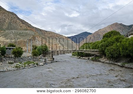 The Bridge Across Fast, Affluent And Muddy Mountain Nepal River Near Jomsom Village