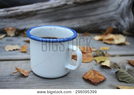 A White Mug With Coffee On A Wooden Table With Autumn Leaves.