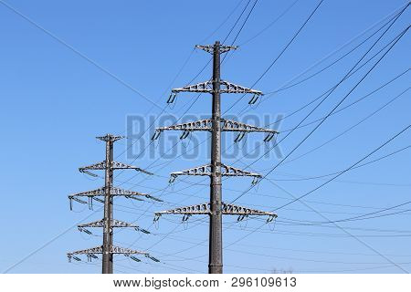 Power Line Supports With Electrical Wires On Clear Blue Sky Background. High Voltage Electricity Tra