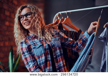 Smiling Cheerful Woman In Glasses And Checkered Shirt Chooses Clothes In Butique  For Her Holidays. 