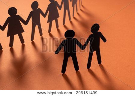 Black paper figure of male couple in front of a crowd of paper people holding hands on redsurface. Social movement, protest, minorities concept.