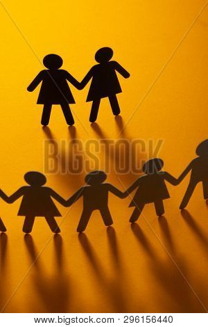 Black paper figure of a female couple in front of a crowd of paper people holding hands on orange background. Social movement, minorities, same-sex marriage concept.