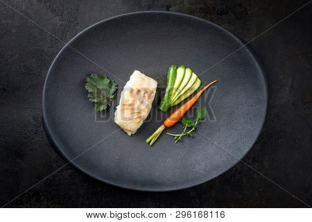 Fried Danish skrei cod fish filet with baby zucchini, carrot and lettuce as top view on a modern design plate 