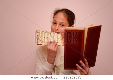 Portrait Of The Cute Teenager Girl Holding Matzah And Reads The Passover Haggadah. Jewish Child Eati