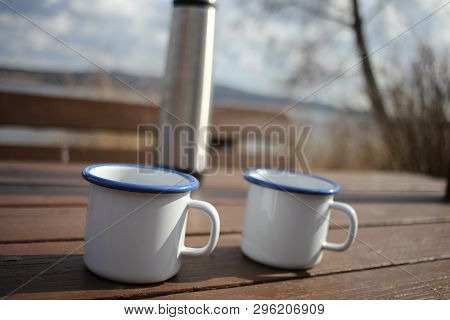 Two Coffee Cups And A Thermos Blurred In The Background. Picknick Outdoors.