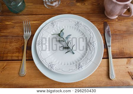 On The Wooden Table Is A White Plate, On It Is A Plate With Patterns On The Edges. At The Top Is A G