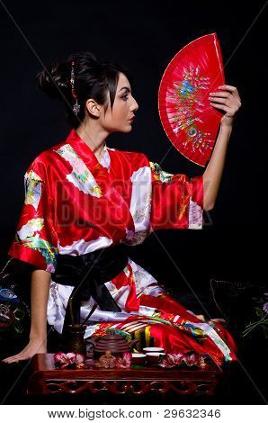Woman in red Asian costume arranging Japanese tea ceremony