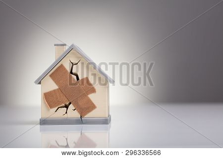 Broken House Model With Crossed Band Aid On Desk