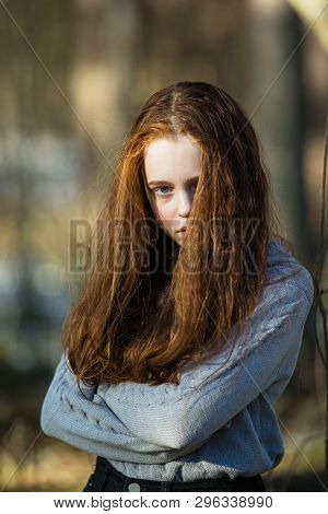 Cute teengirl with long bright red hair posing for camera outdoors.