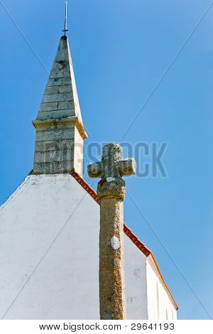 Starý kamenný kříž a střecha kaple země s modrou oblohou na pozadí