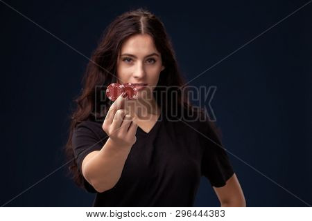 Curly Hair Brunette Is Posing With Red Gambling Chips In Her Hands. Poker Concept On A Black Backgro