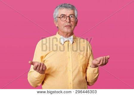 Studio Shot Of Handsome Old Man Wearing Yellow Shirt, White Bow Tie, And Glasses, Has Serious Facial