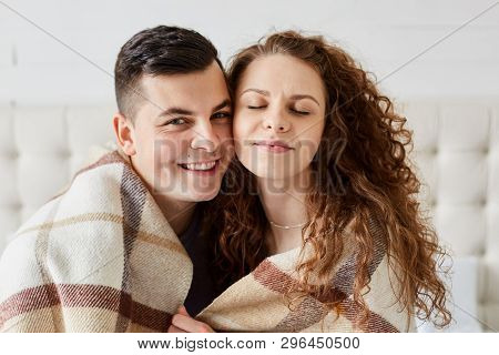 Portrait Of Cute Happy Couple Sitting In Bed Embrace Each Other. Beautiful Girl With Long Curly Hair