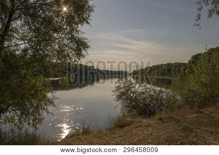 Wide River Flowing Across Green Forest. Fall. Evening. Reflections Of Sun In The Water