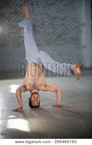 An Athletic Man On Capoeira Training. Standing On The Hands And Head