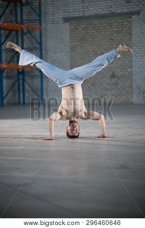 An Athletic Man On Capoeira Training. Standing On The Hands With Legs Apart
