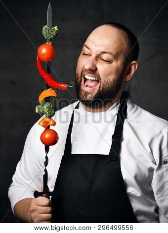 Bearded Professional Chef In White Skirt And Apron Going To Eat Vegetables On A Skewer Kebab On Kitc