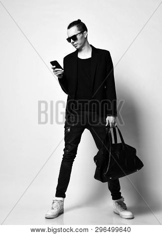 Young Modern Man With A Bun On Head In Sunglasses And With A Big Bag Is Typing A Message Or Read New