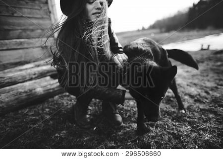 Happy Young Woman Plaing With Her Black Dog In Fron Of Old Wooden House. Black And White Photo