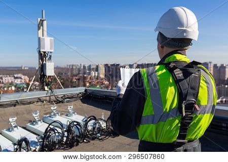 Professional Industrial Climber In Helmet And Uniform Reads Technical Documentation And  Antennas Of