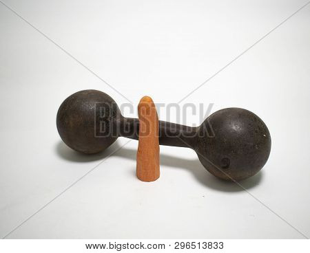 Very Old Rusty Heavy 17 Pound Iron Dumbbell And Standing Next To It A Peeled Carrot On A White Backg
