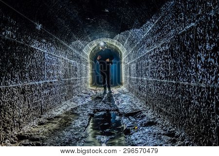 Sewer Worker Examines Dark Underground Sewer Tunnel