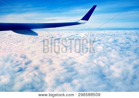 The Blue Wing Of A Large Airplane, Flying Over The White Morning Clouds, At High Altitude Above The 
