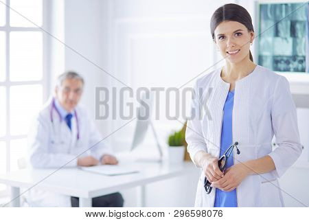 A Doctor Looking At The Camera With Her Male Colleage In The Back Of The Conference Room In Hospital