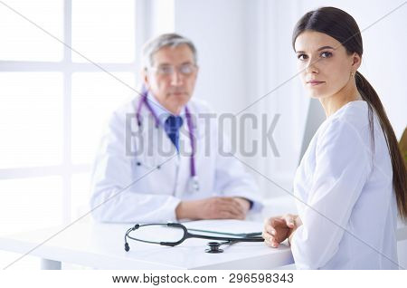 A Doctor Looking At The Camera With Her Male Colleage In The Back Of The Conference Room In Hospital