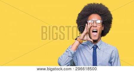 Young african american business man with afro hair wearing glasses shouting and screaming loud to side with hand on mouth. Communication concept.