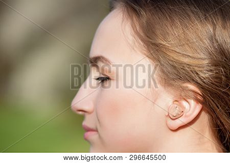 Close-up Of Female Hands Putting Hearing Aid In Ear. Modern Digital In The Ear Hearing Aid For Deafn