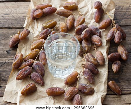 Dried Dates Fruits On A Branch And A Glass Of Water On A Wooden Table. Traditional Fast Breaking, Mu