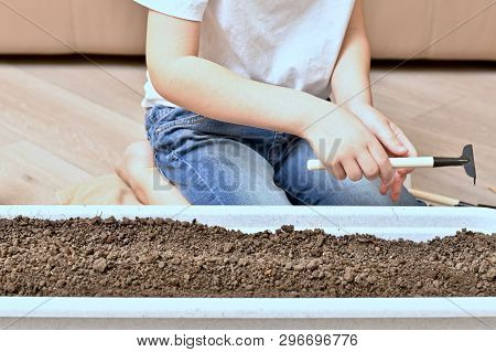 A Child With A Rake Prepared For Work With The Earth In Pots.