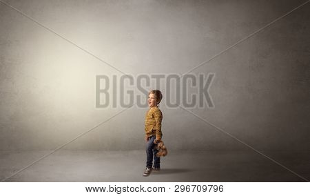 Little waggish kid staying alone in a big empty room with his plush