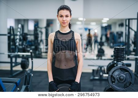 Beautiful Young Woman In Black Spotswear Standing In The Gym And Looking At Camera. Attractive Model