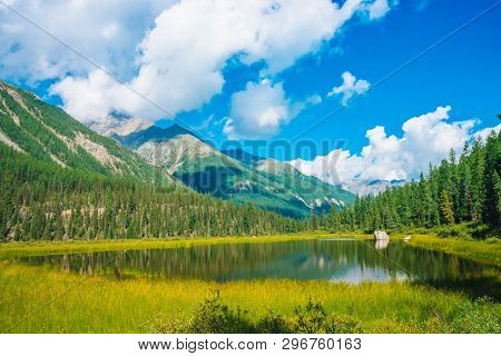 Beautiful Mountain Lake Before Giant Mountains Under Blue Sky With White Clouds. Forest Edge On Slop