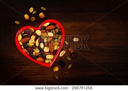 Energy Blend Trail Mix With Nuts And Dried Fruits In Heart Shaped Bowl On Wooden Background. Selecti