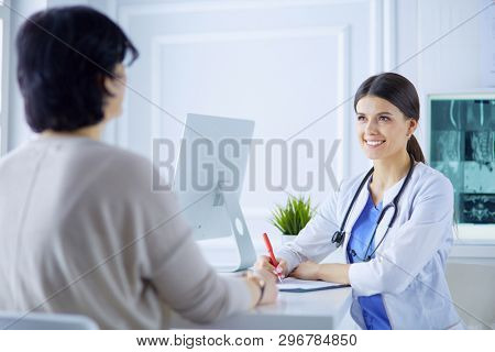 Doctor and patient discussing medical problems in a hospital consulting room. Doc filling in a patient's form