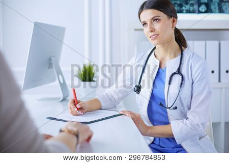 Doctor and patient discussing medical problems in a hospital consulting room. Doc filling in a patient's form