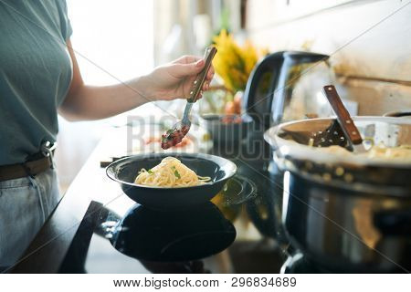 Contemporary young woman adding hot sauce on to pof spaghetti pile in bowl before enjoying real italian pasta