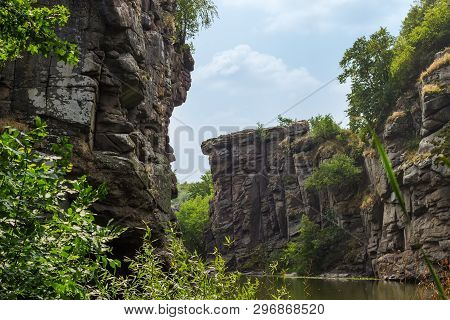 Gloomy Overhanging Cliffs On The Banks Of Calm River Flowing In Canyon At Summer Day. Buky Canyon, U