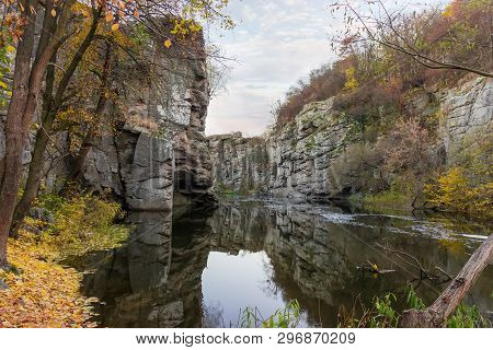 Gloomy Overhanging Cliffs On The Banks Of Calm River Flowing In Canyon At Late Autumn. Buky Canyon, 
