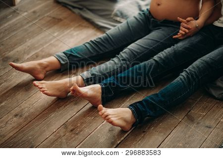 A Man And His Pregnant Wife Sit On The Wooden Floor And Holg Hands.