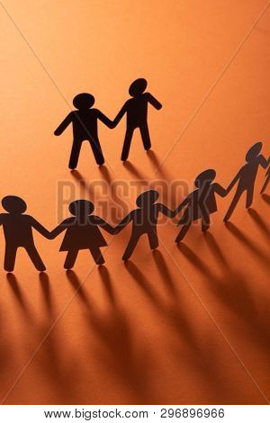 Black paper figure of male couple in front of a crowd of paper people holding hands on redsurface. Social movement, protest, minorities concept.