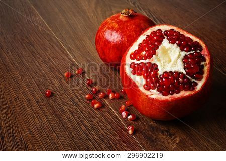 Stil Life - Red Whole And Cutted Pomegranate Fruits And Scattered Seeds On A Dark Wooden Tabletop